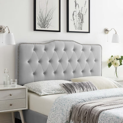 Light gray upholstered, diamond-tufted headboard with nailhead trim in a stylish bedroom.
