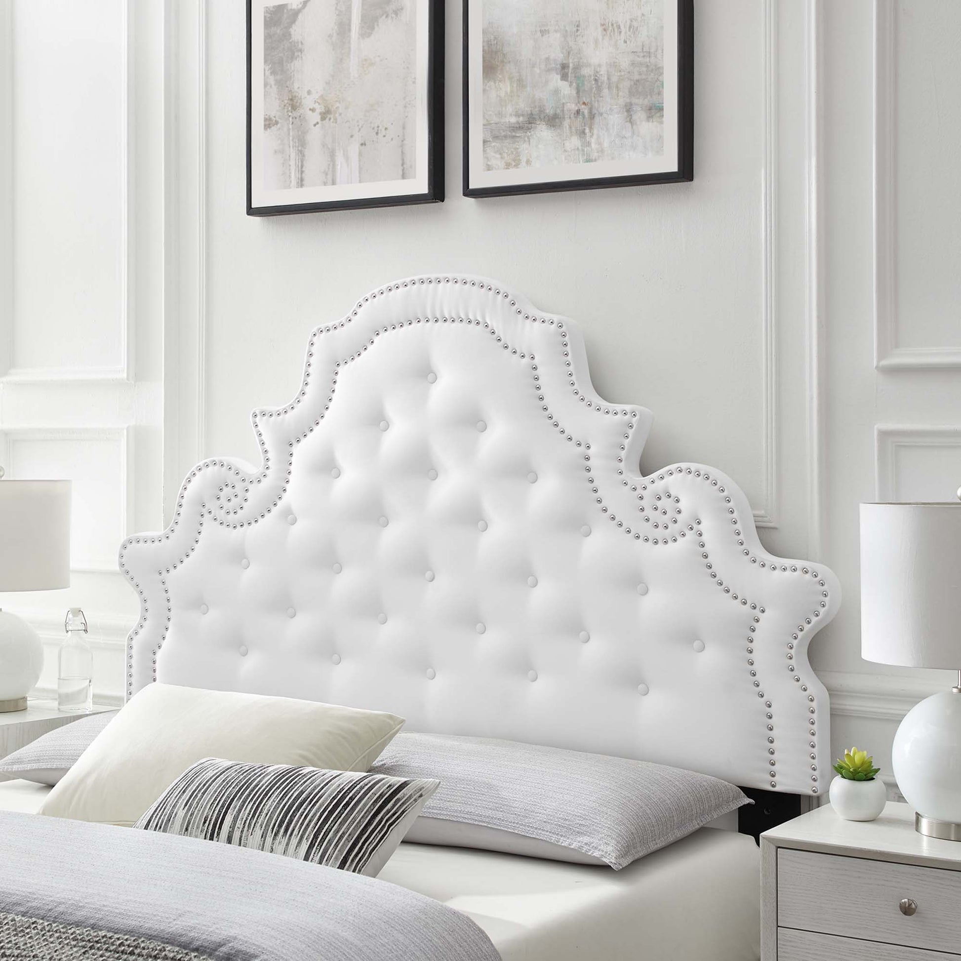 White tufted fabric headboard with scalloped Rococo silhouette and silver nailhead trim, glam bedroom centerpiece.