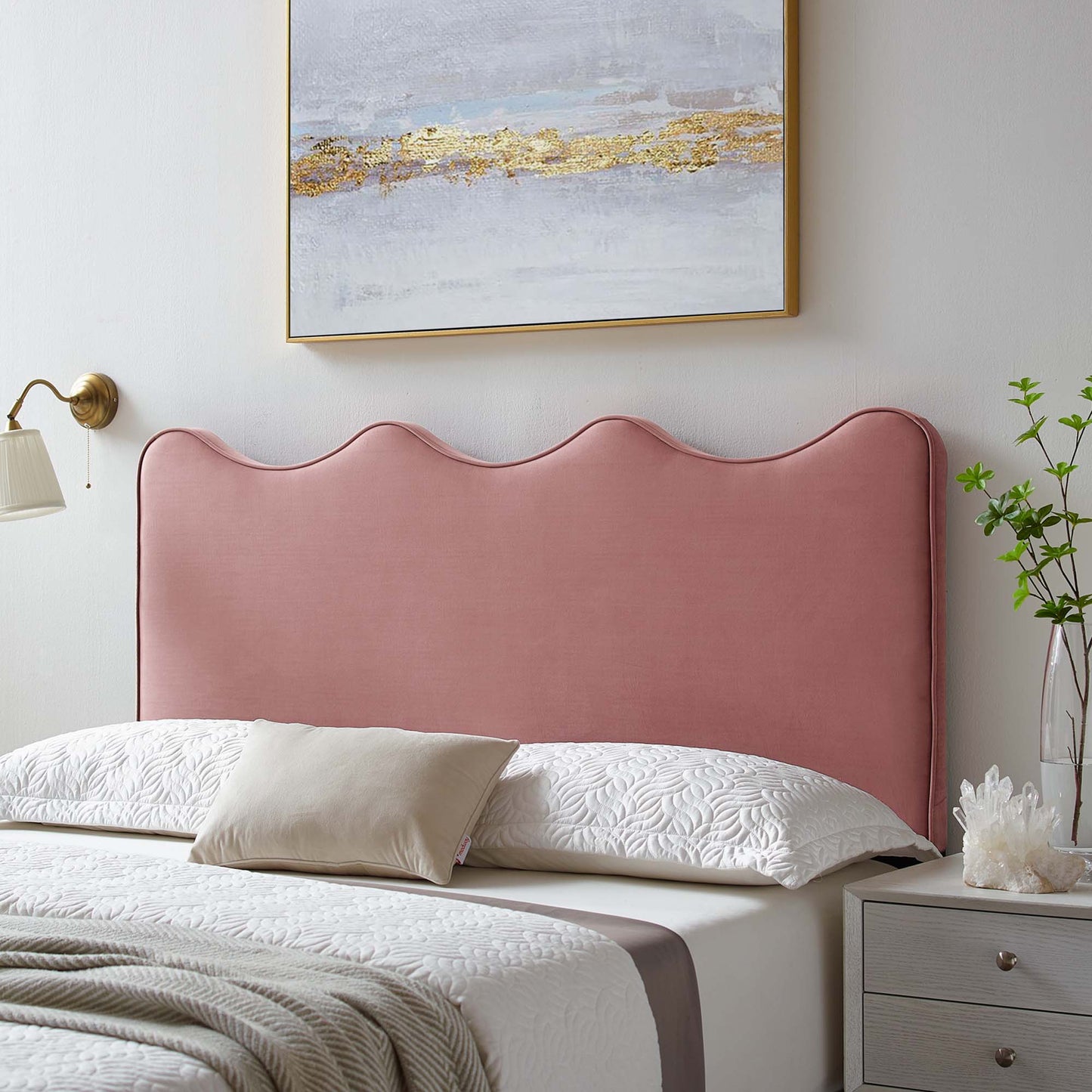 Red velvet twin headboard with a scalloped top, white quilted bedding, beige pillow, brass wall lamp, gray nightstand.
