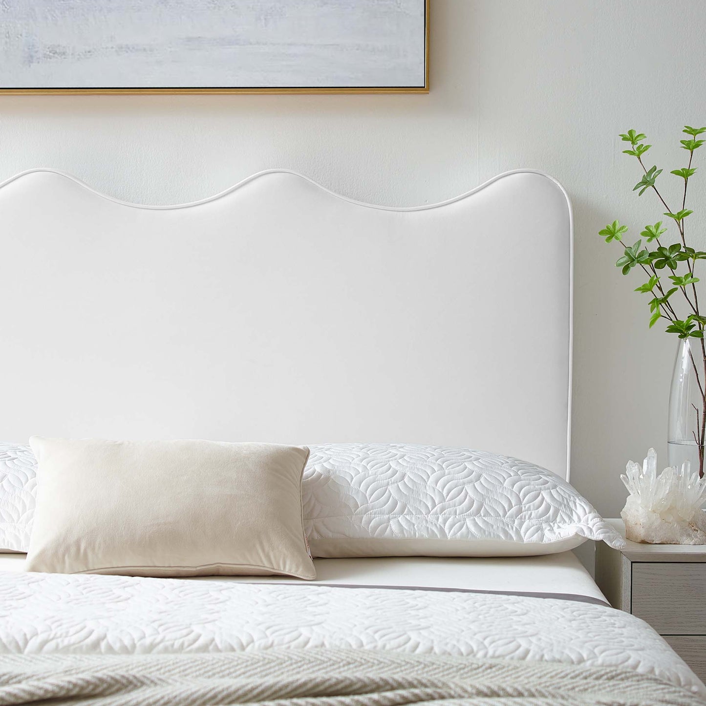 White scalloped upholstered twin headboard with quilted white bedding and beige lumbar pillow in a serene bedroom