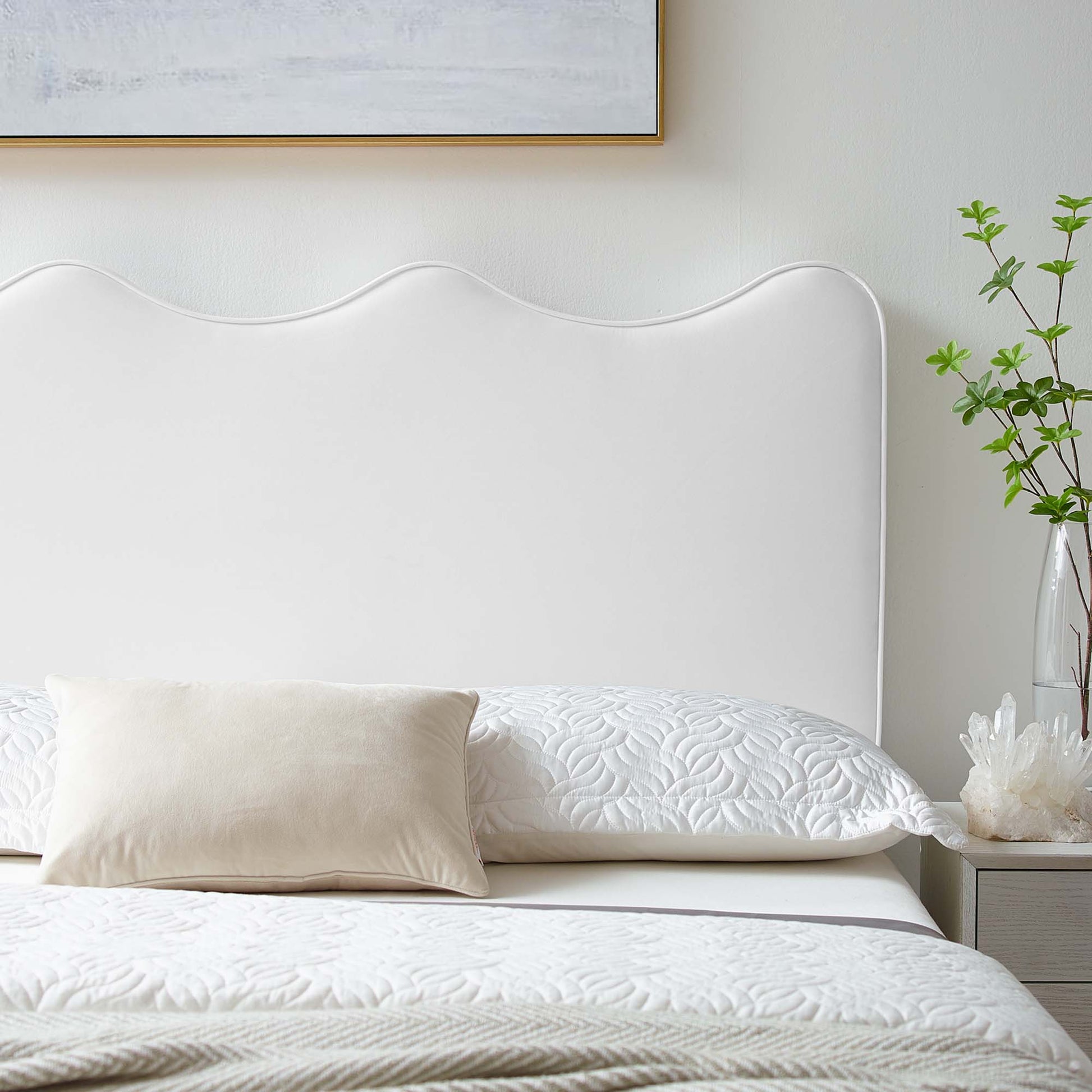 White scalloped upholstered twin headboard with quilted white bedding and beige lumbar pillow in a serene bedroom