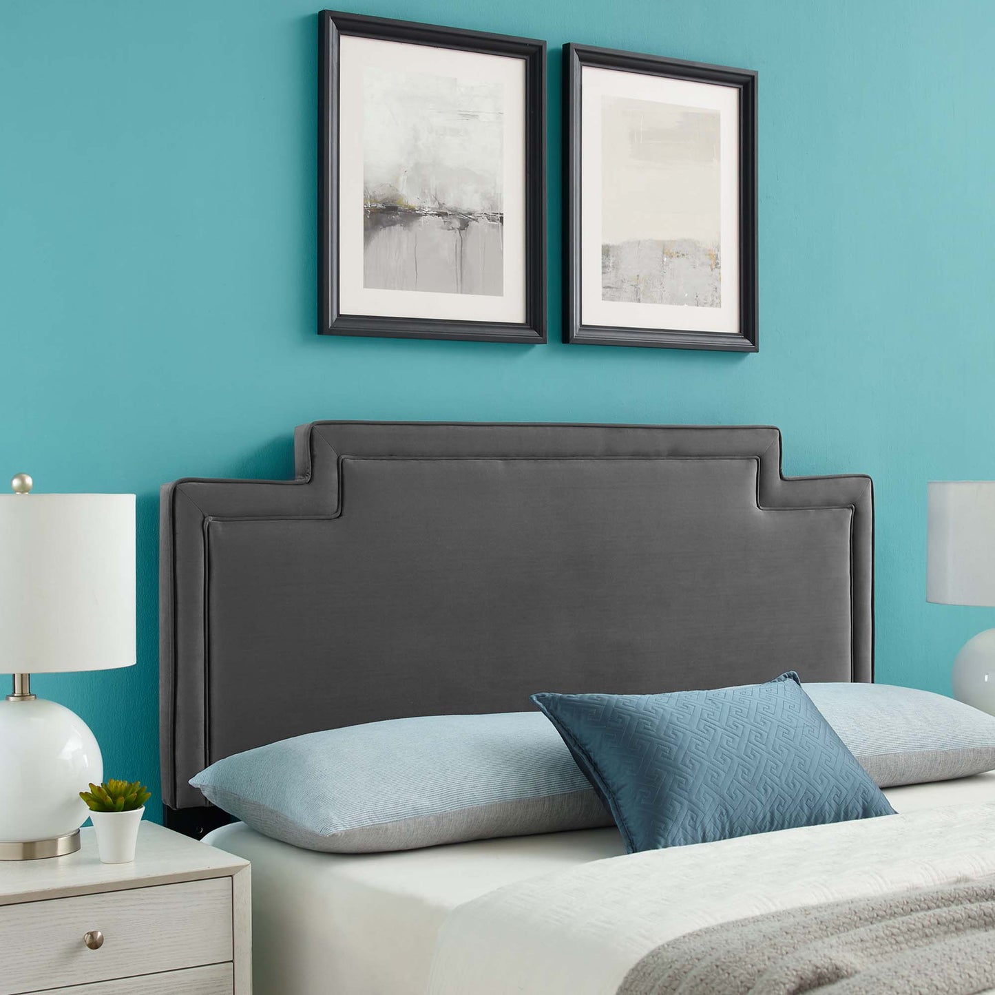 Grey upholstered headboard with stepped edges on teal wall; two framed abstract prints, light blue bedding, white nightstands.
