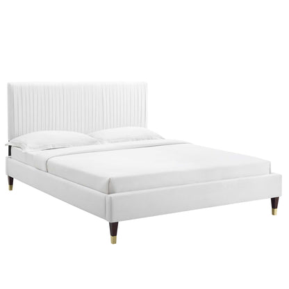White upholstered platform bed with tall vertical channel-tufted headboard, low base & tapered wooden legs.
