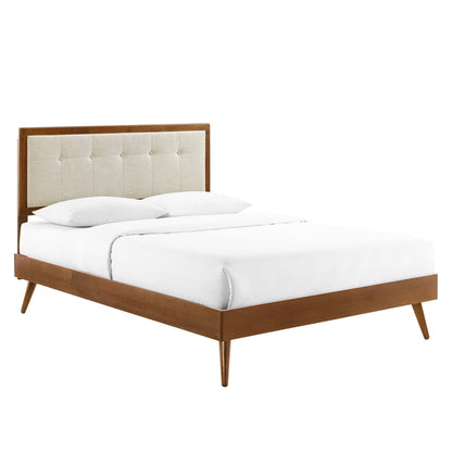 Mid-century walnut bed with tufted beige fabric headboard, tapered legs, and white linens.