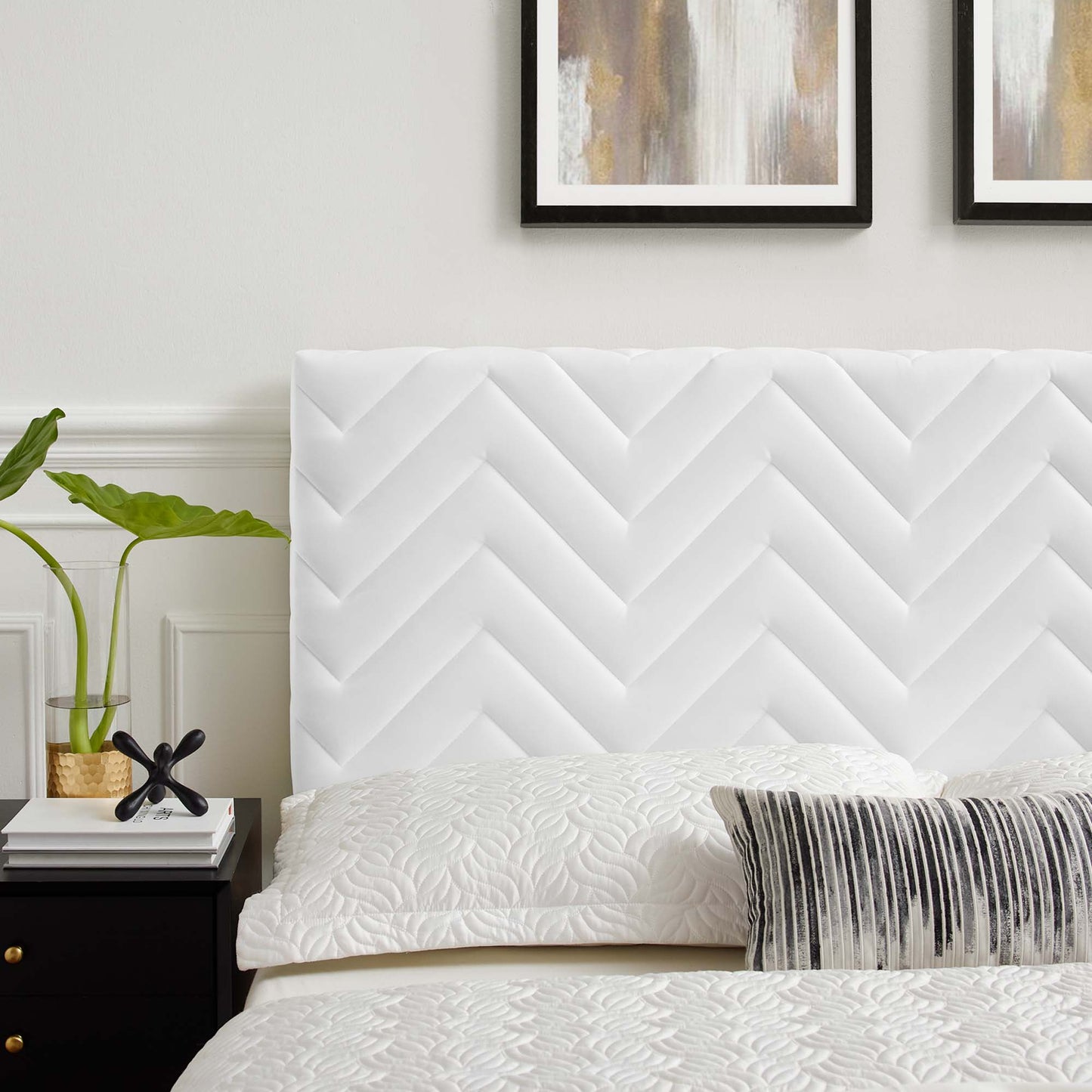 White chevron headboard with quilted bedding and a gray striped lumbar pillow in a modern bedroom; plant on a nightstand.