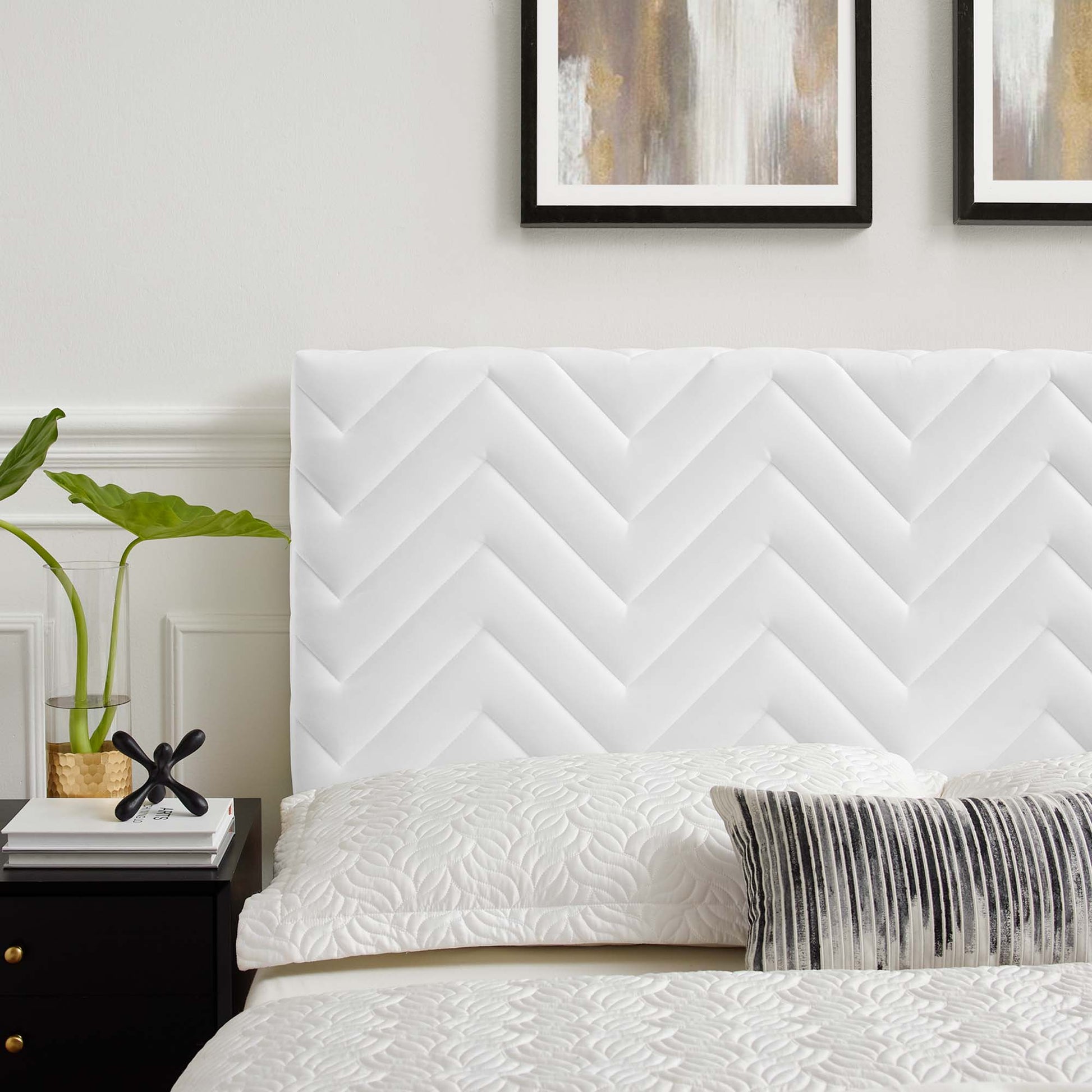 White chevron headboard with quilted bedding and a gray striped lumbar pillow in a modern bedroom; plant on a nightstand.