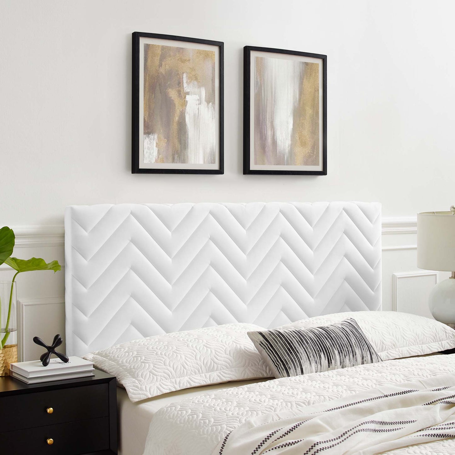 White tufted chevron headboard with quilted linens, black nightstand, plant, and two abstract framed artworks above.