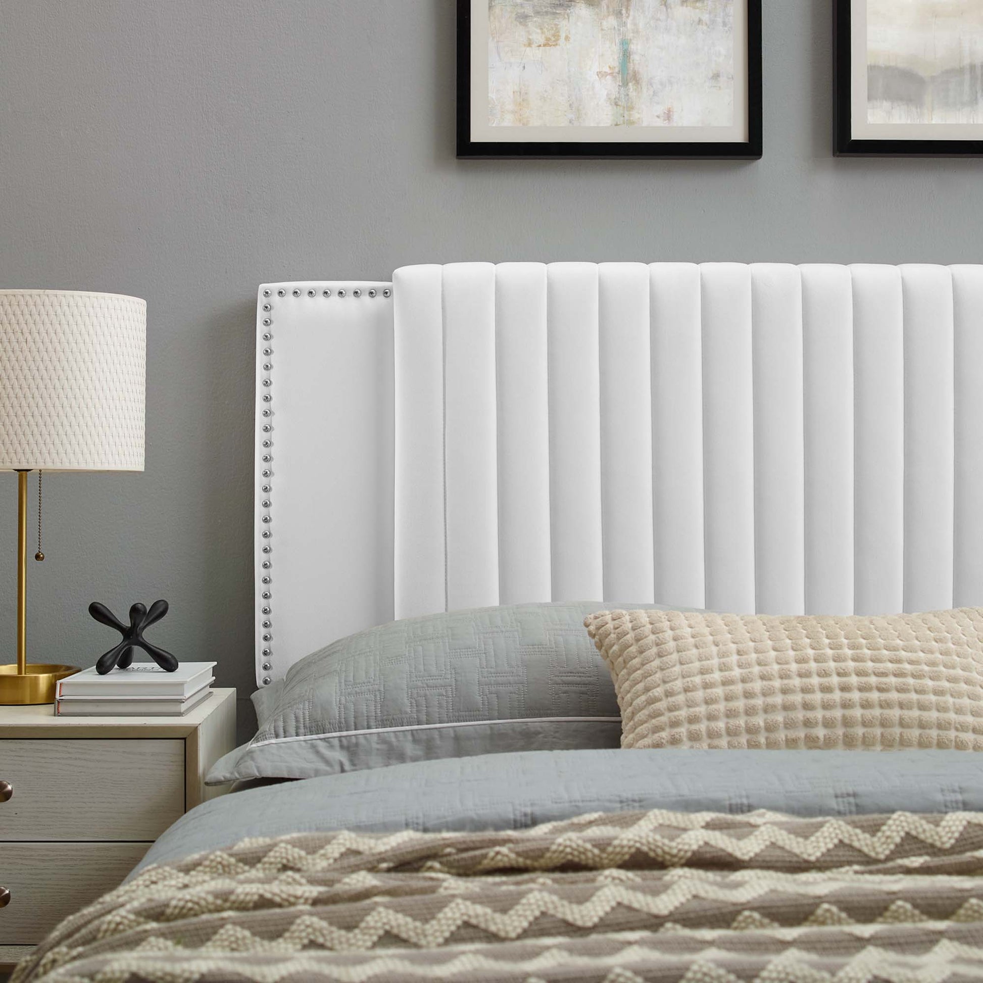 White channel-tufted headboard (twin) against grey walls with blue-gray bedding, beige textured throw, and a lamp and books beside the bed.