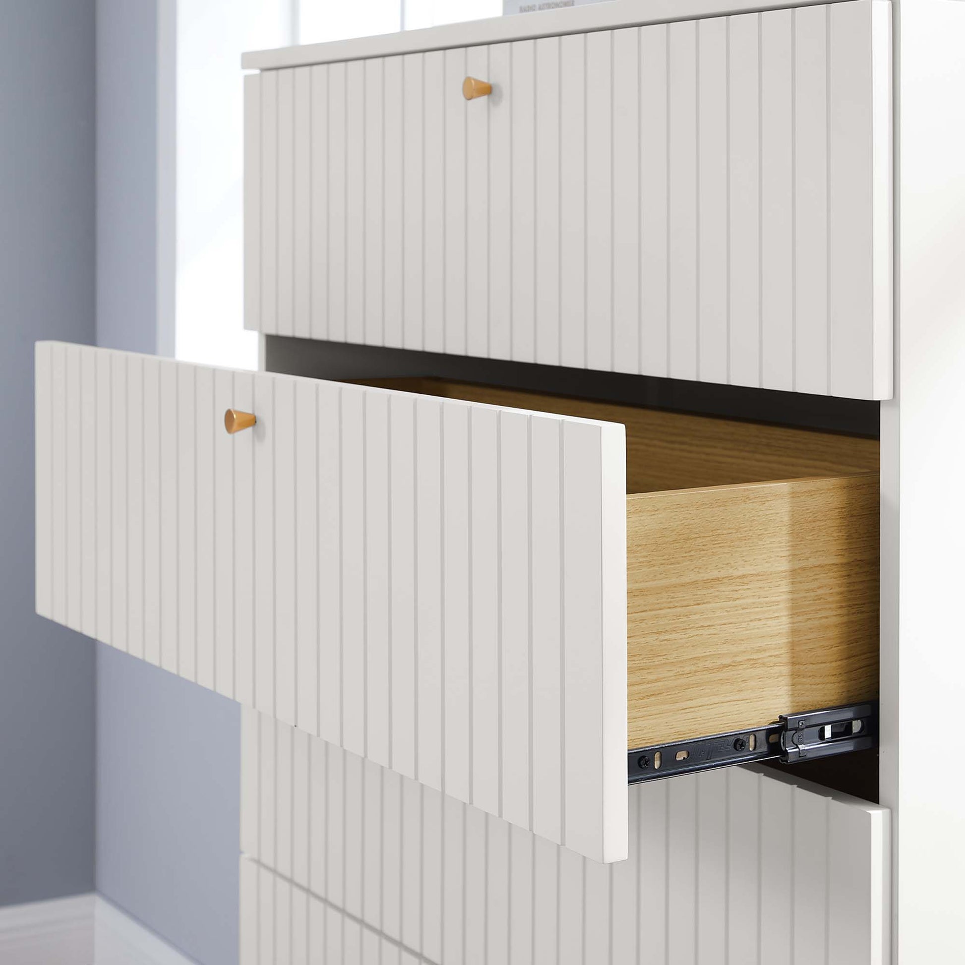White ribbed-drawer chest with amber knobs; middle drawer pulled out to reveal light oak interior and metal slides.