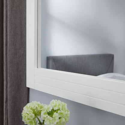 White framed wall mirror with clean lines; reflects gray headboard, dark curtain, and pale green hydrangea in foreground.
