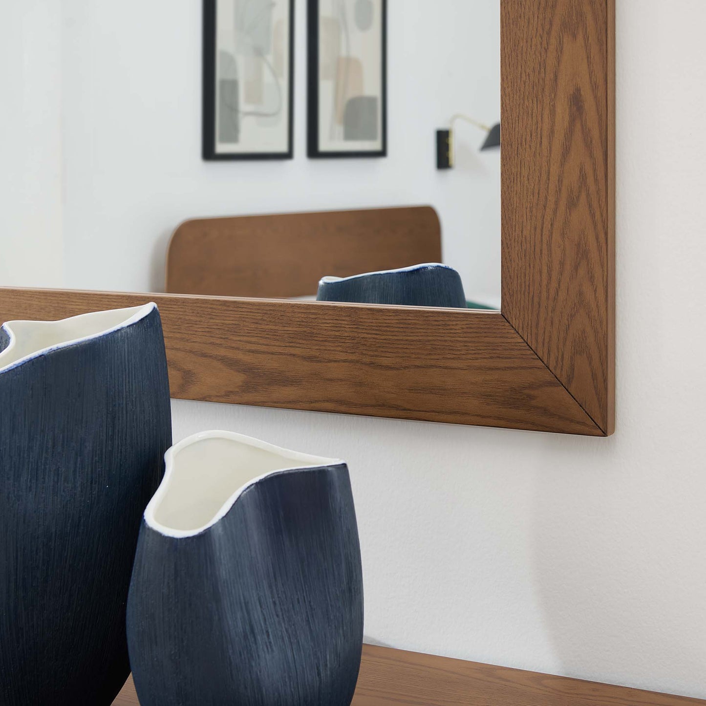 Walnut-framed rectangular wall mirror above a wooden surface, with two navy ceramic vases featuring white rims.