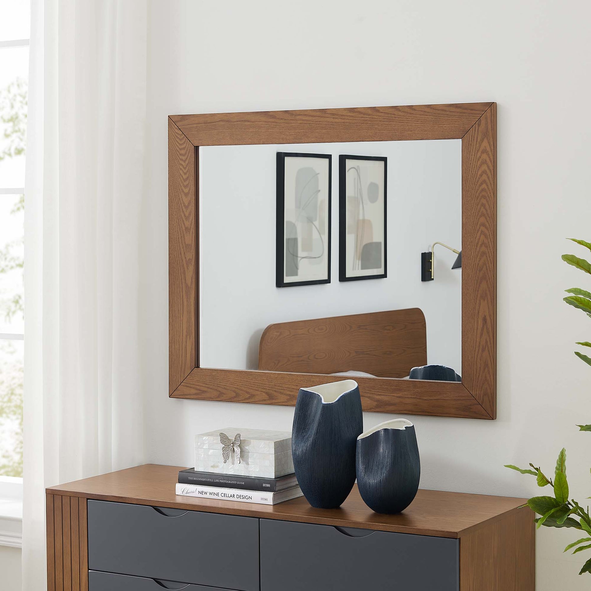 Walnut-framed rectangular mirror above a walnut console with gray drawers, featuring two navy ceramic vases and stacked books