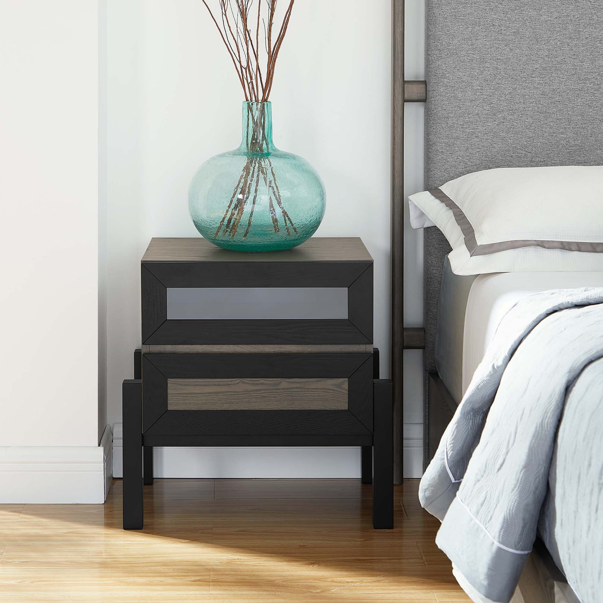 Modern two-drawer nightstand in dark wood with oak fronts, topped by a turquoise glass vase with branches.