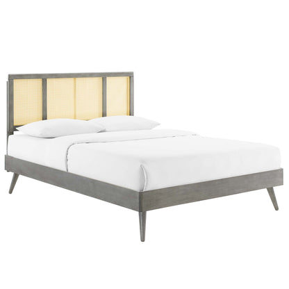 Gray wood platform bed with cane-panel headboard & splayed legs, white bedding; modern rustic bedroom centerpiece.