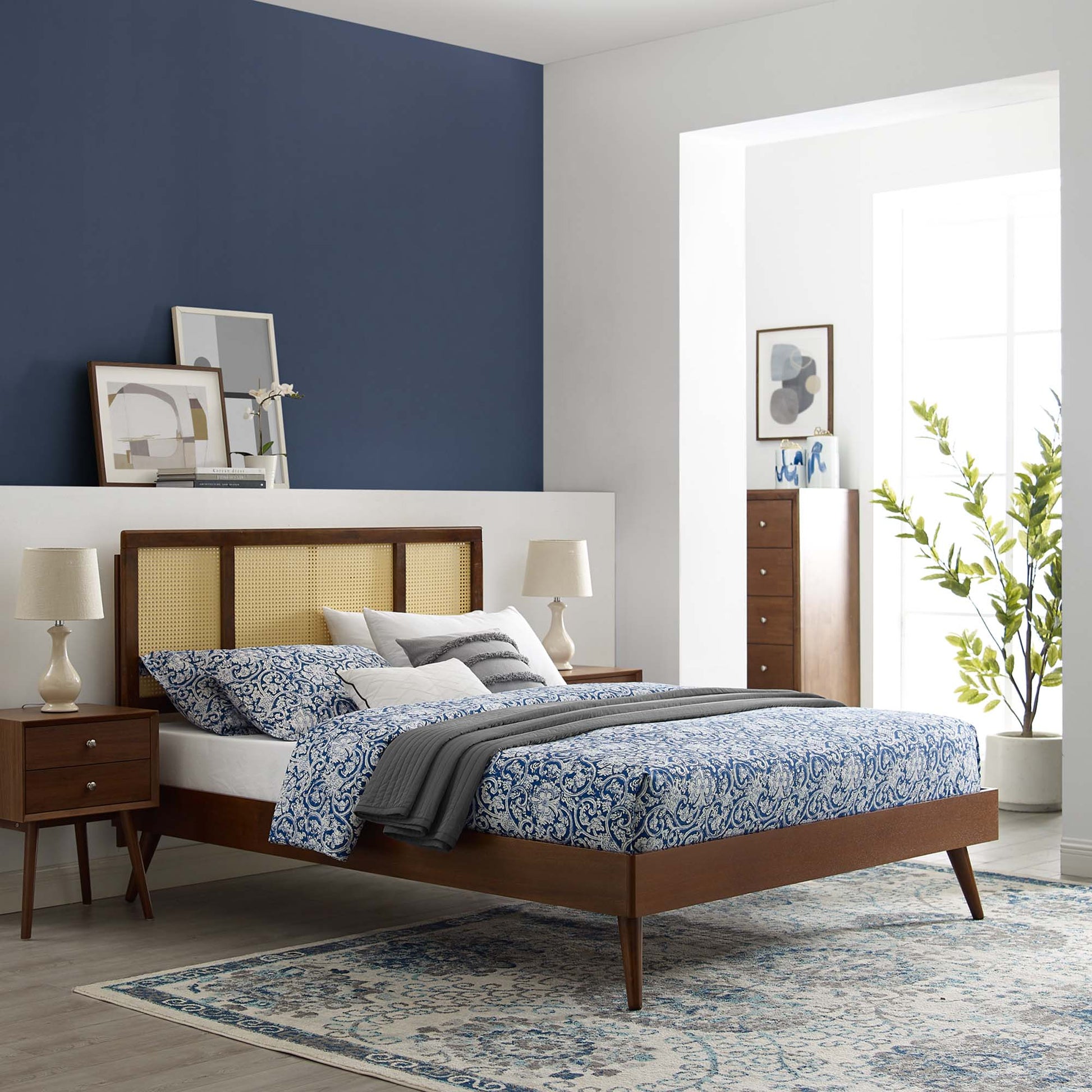 Walnut bed with cane headboard, blue patterned bedding, grey throw, matching nightstands, warm lighting in a bedroom.