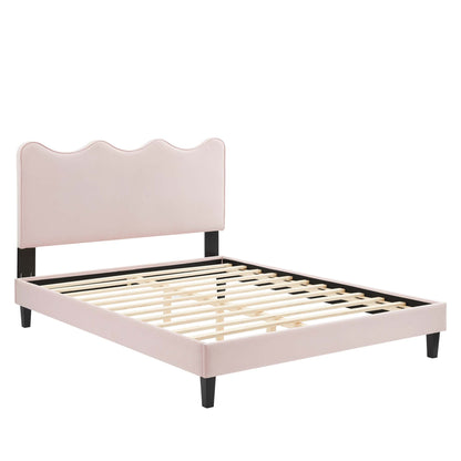 Blush pink upholstered platform bed frame with scalloped headboard, black legs, and wooden slats.