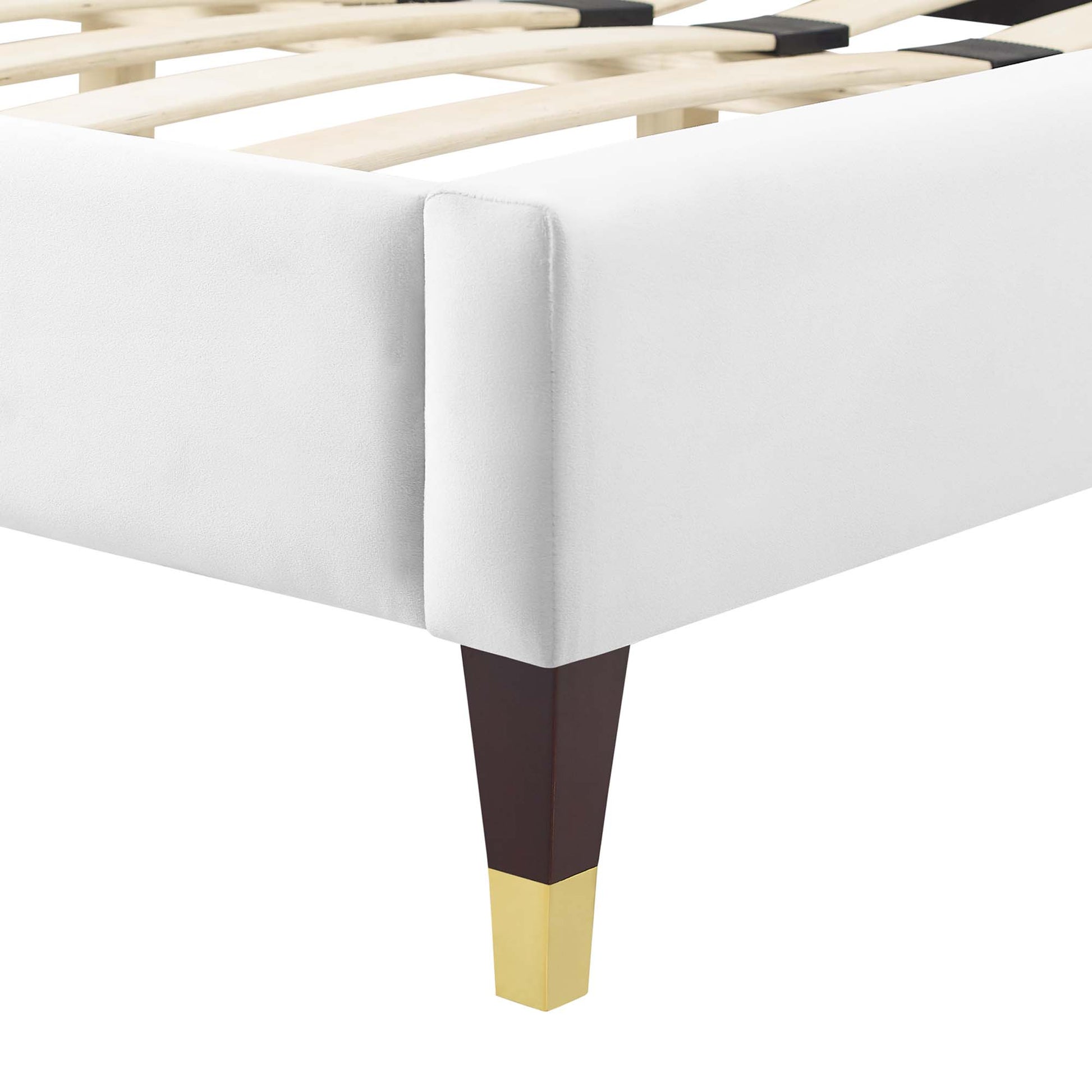 White upholstered platform bed with wooden slats and dark tapered legs with gold caps.