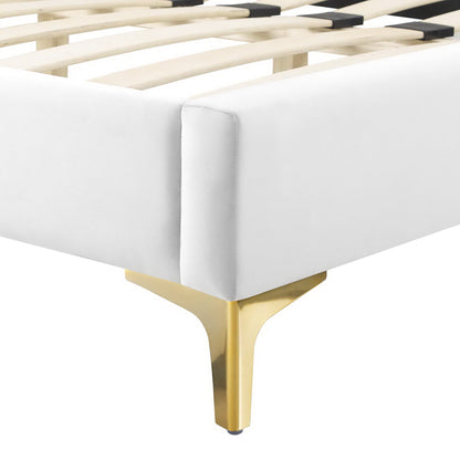 White upholstered platform bed with a gold metal leg and wooden slat base, corner view.