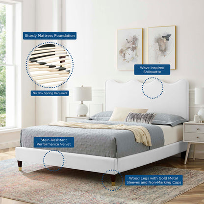 White upholstered platform bed with wave-inspired curved headboard, velvet fabric, wooden legs with gold sleeves.