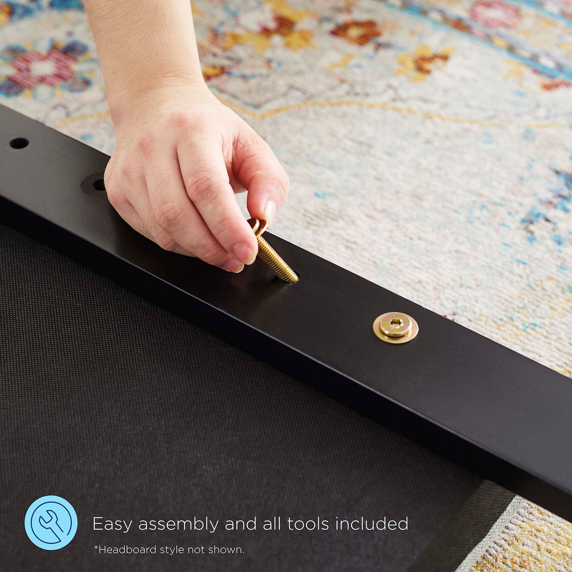 Close-up of a hand tightening a gold brass bolt into a sleek black metal frame on a patterned rug.