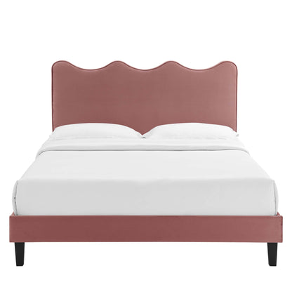 Dusty-rose upholstered bed with scalloped wave headboard, low platform frame, black tapered legs, and white bedding.