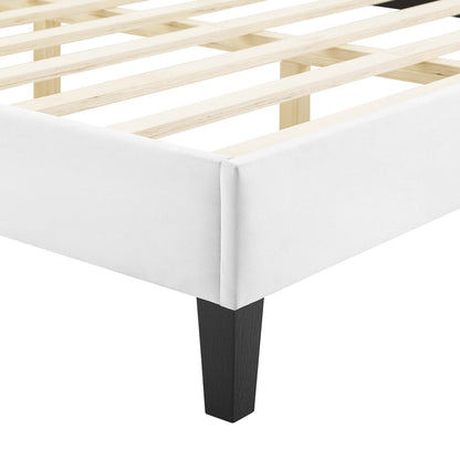White upholstered platform bed frame corner with natural wood slats and a black tapered leg.