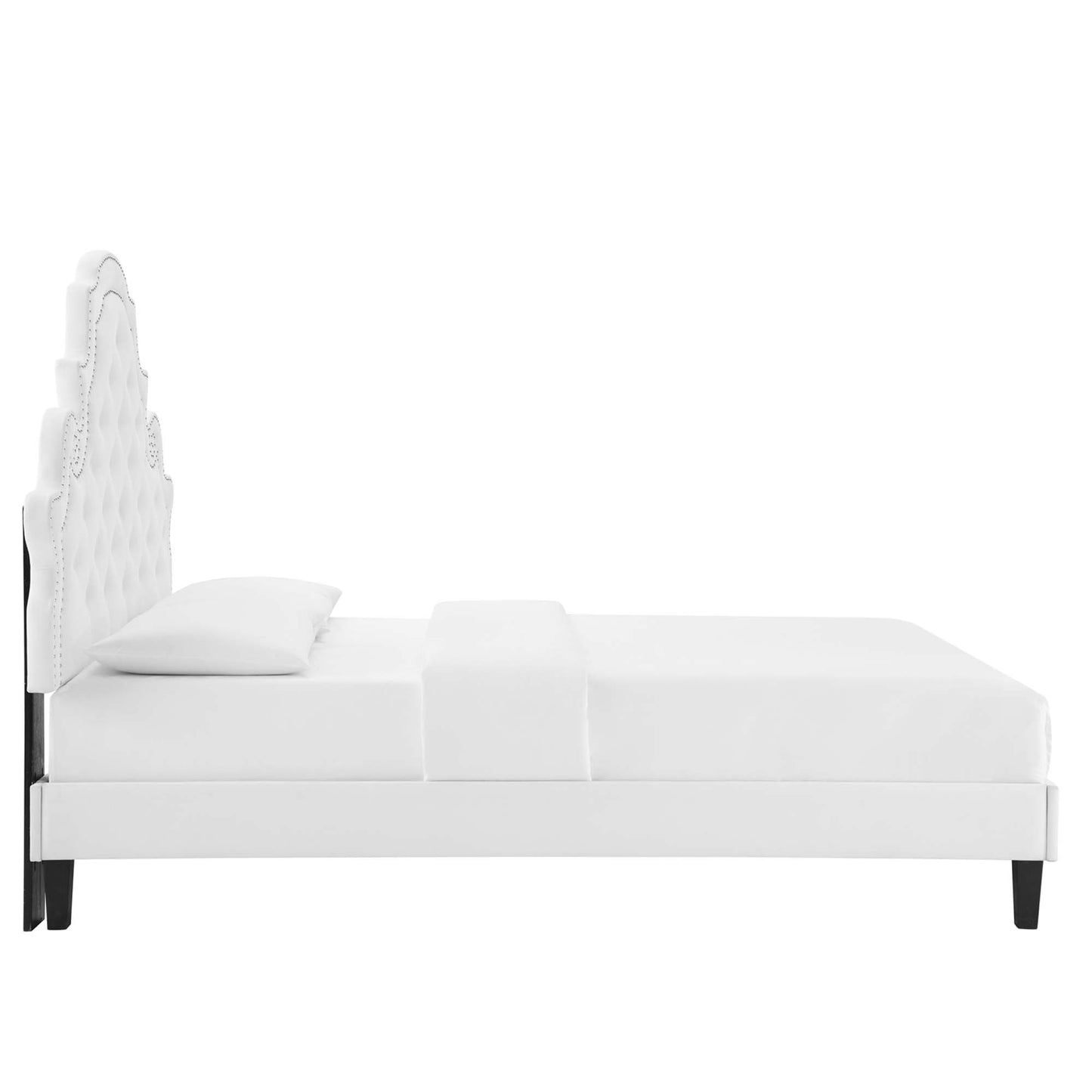 White upholstered bed with tall tufted headboard, curved ornate detail, platform frame, dark tapered legs.