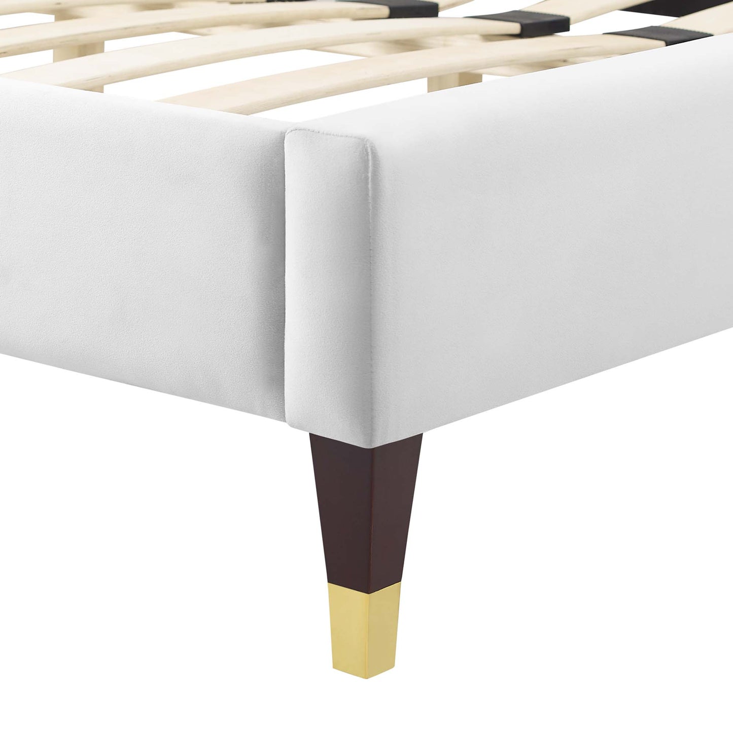 White upholstered bed frame corner with wooden slats and a tapered dark brown leg with a gold tip.