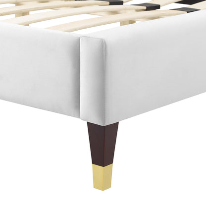 White upholstered bed frame corner with wooden slats and a tapered dark brown leg with a gold tip.