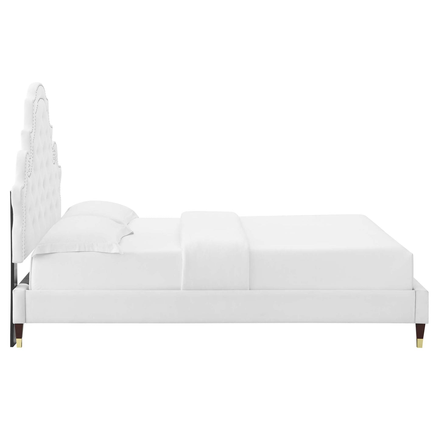 White upholstered full platform bed with tall tufted headboard, dressed in white linens & pillows, gold-tipped legs.