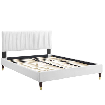 White upholstered platform bed with vertical channel headboard, black accents, wooden slats, tapered legs with brass tips.