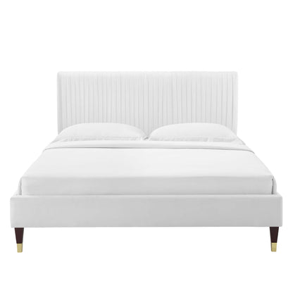 White upholstered platform bed with tall vertical channel-tufted headboard, wood legs with brass caps.