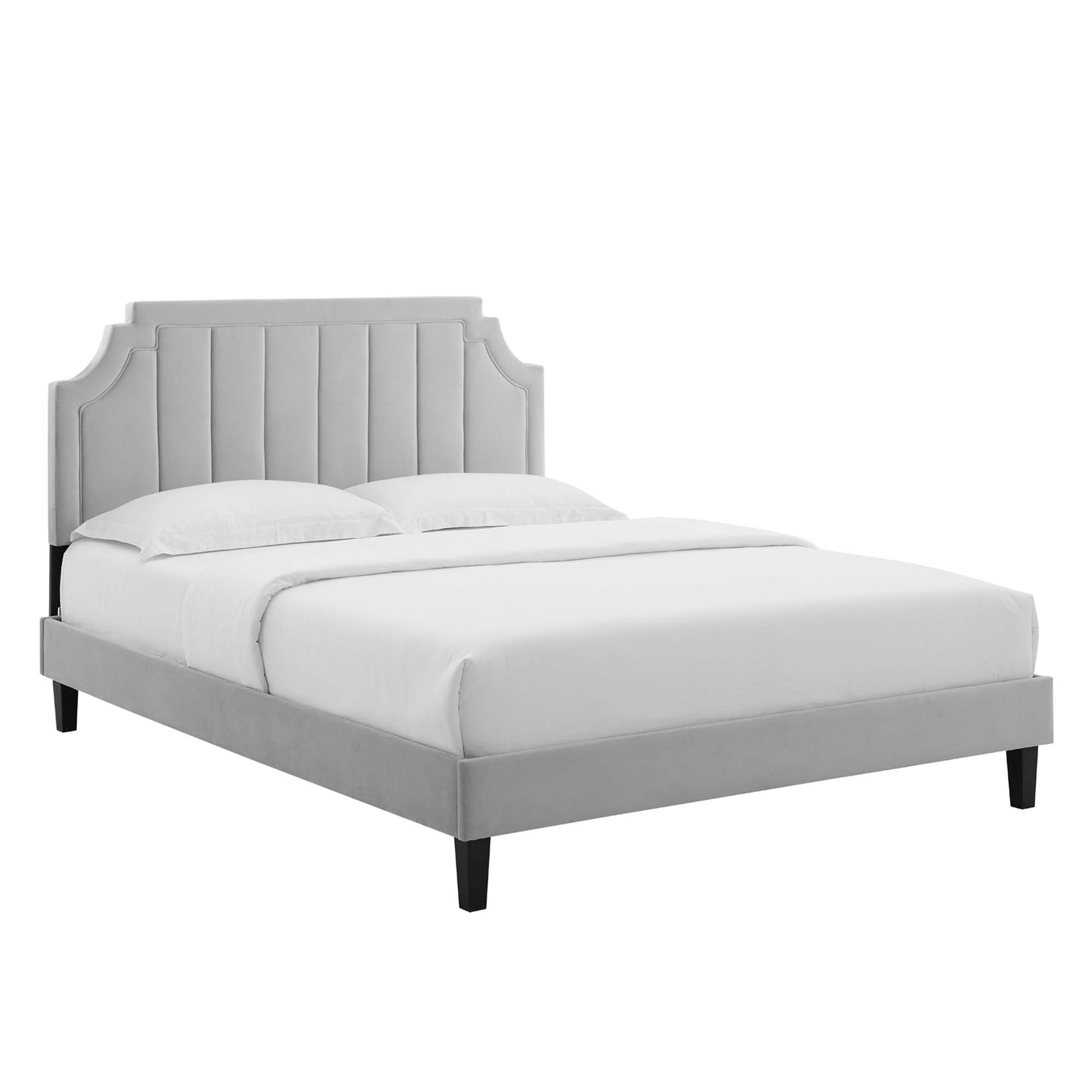 Grey upholstered bed with tall tufted headboard, curved corner accents, low platform frame, black legs, white bedding.