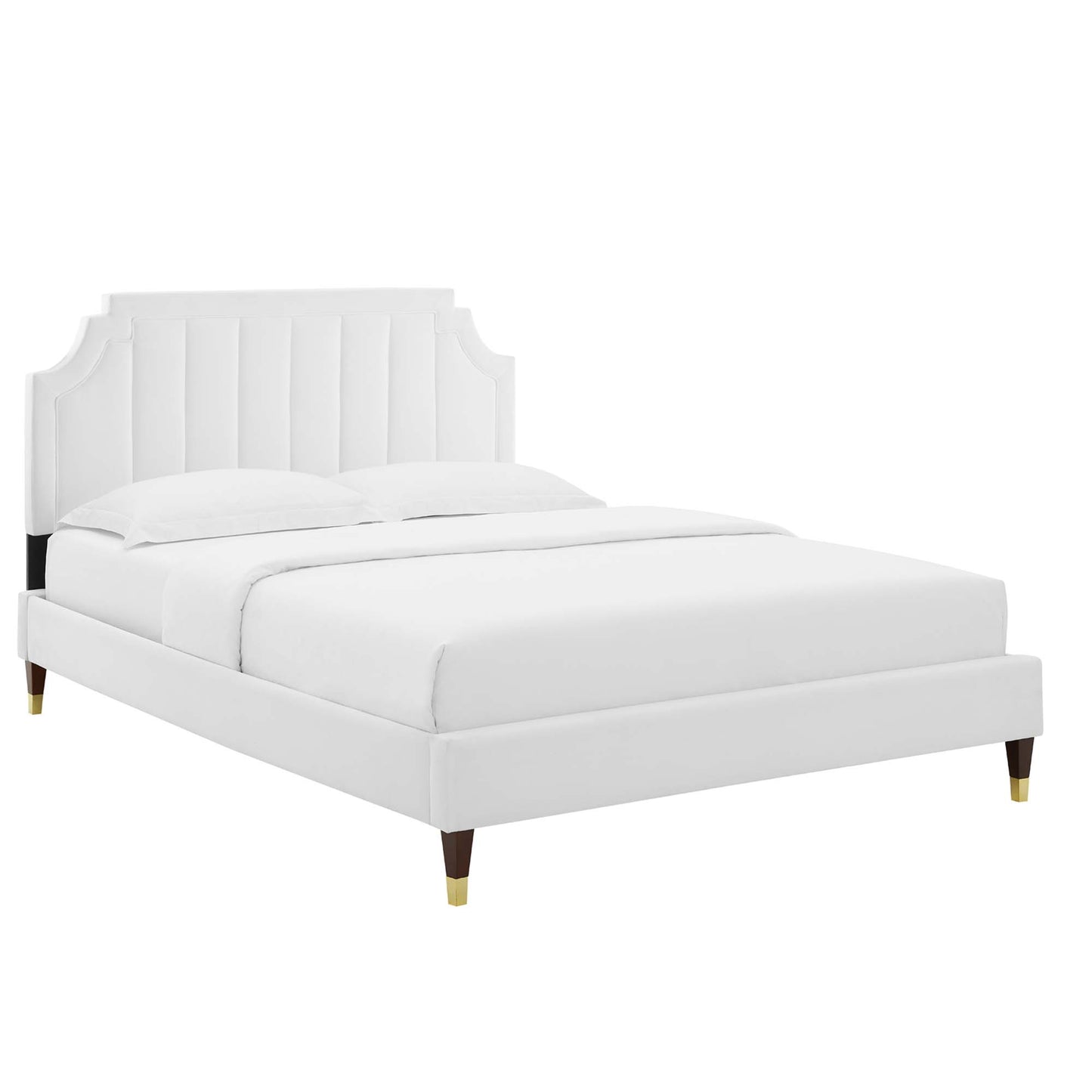 White upholstered platform bed with mattress, vertical channel tufted headboard, and tapered wooden legs with brass caps.