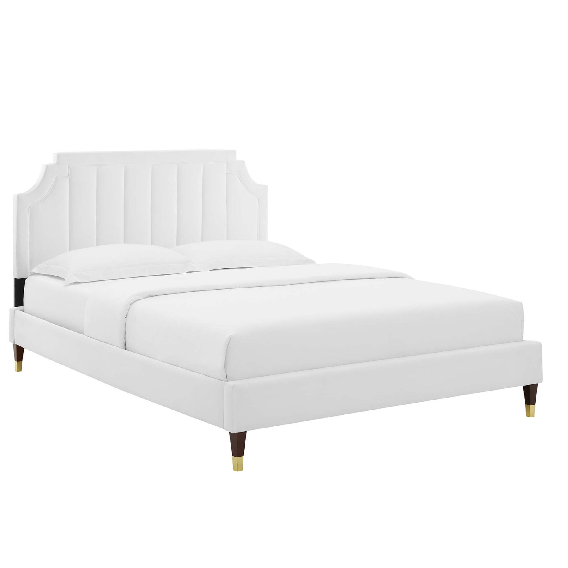 White upholstered platform bed with mattress, vertical channel tufted headboard, and tapered wooden legs with brass caps.