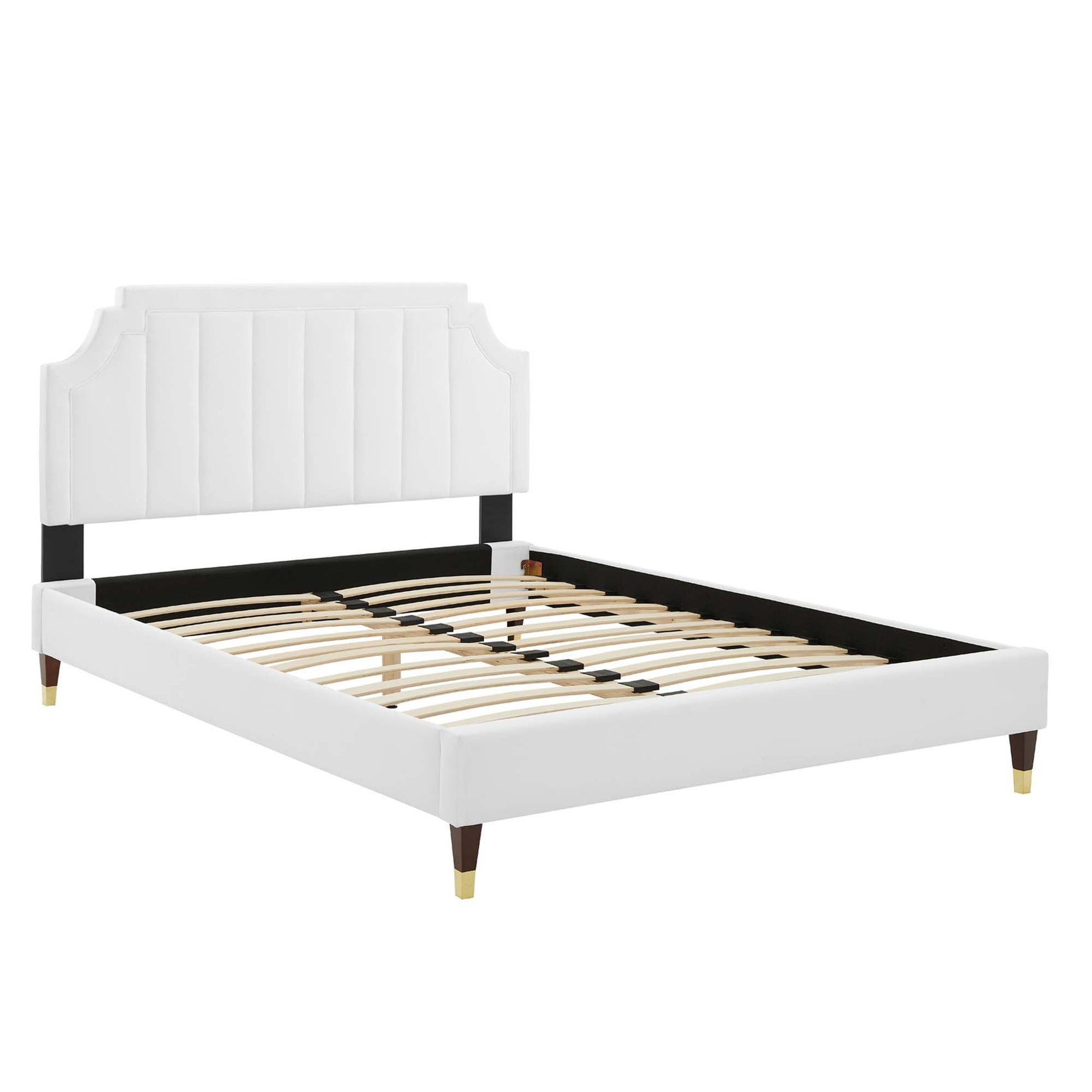 White upholstered platform bed with tall vertically tufted headboard, black rails, wooden slats, & gold-tipped legs.