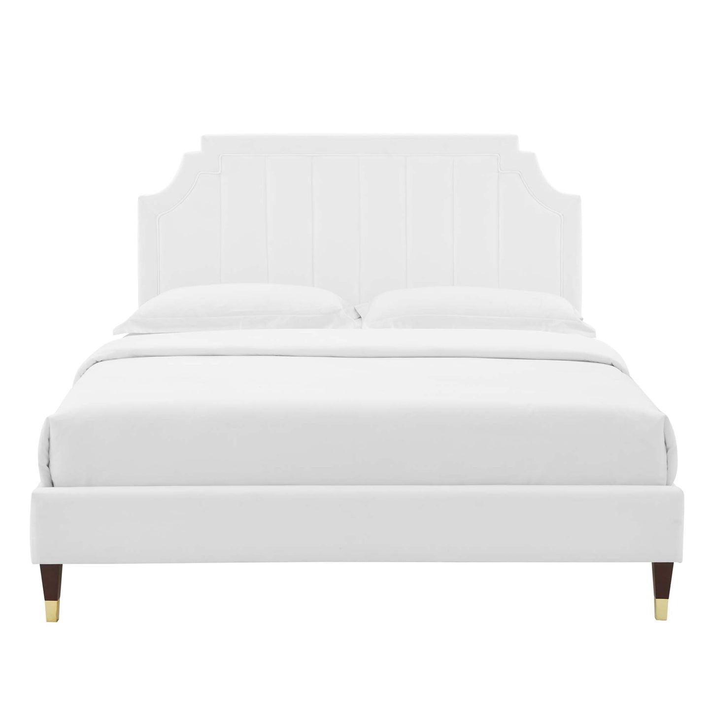 White upholstered platform bed with tall paneled headboard and tapered wooden legs with brass caps, dressed in white bedding.