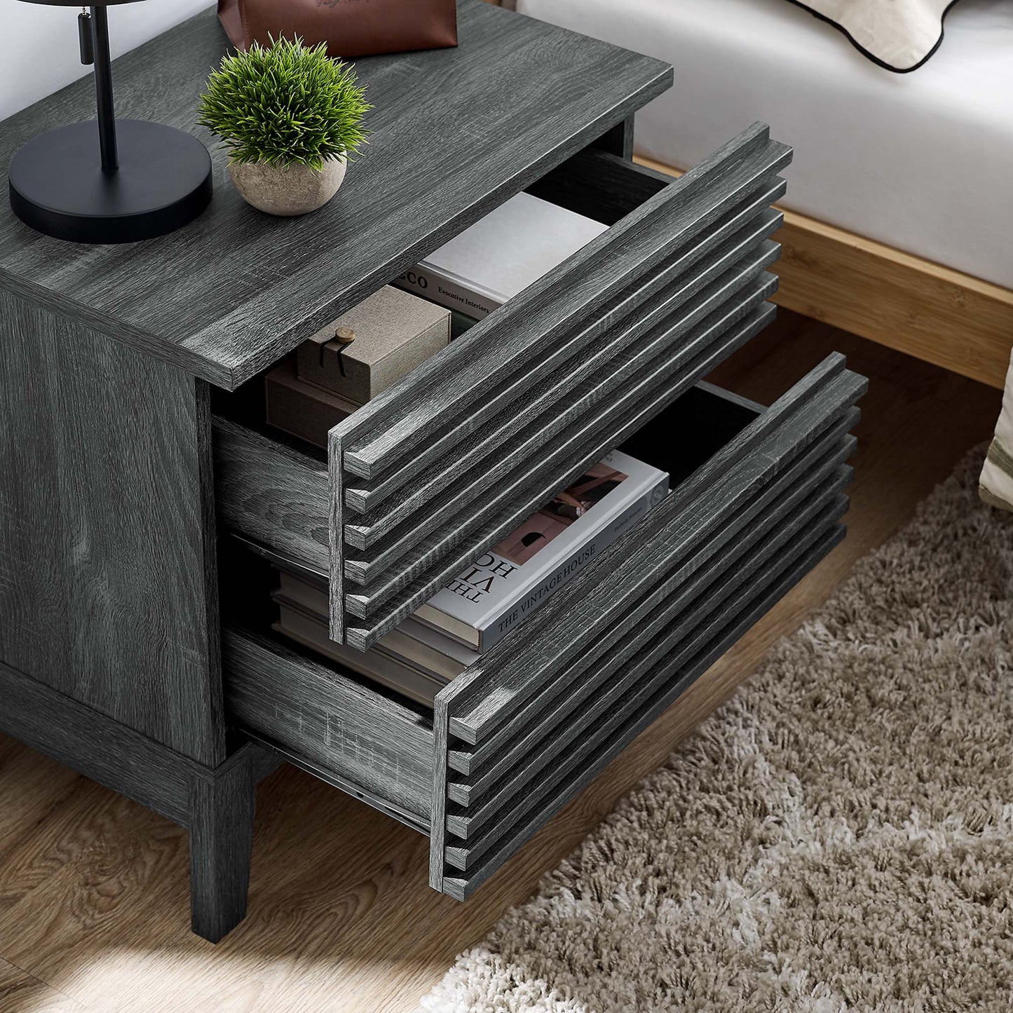 Black two-drawer nightstand with lamp and plant on top; two drawers open with magazines inside.