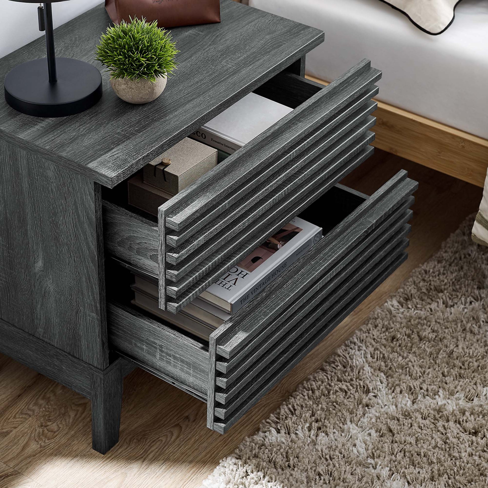 Black two-drawer nightstand with lamp and plant on top; two drawers open with magazines inside.