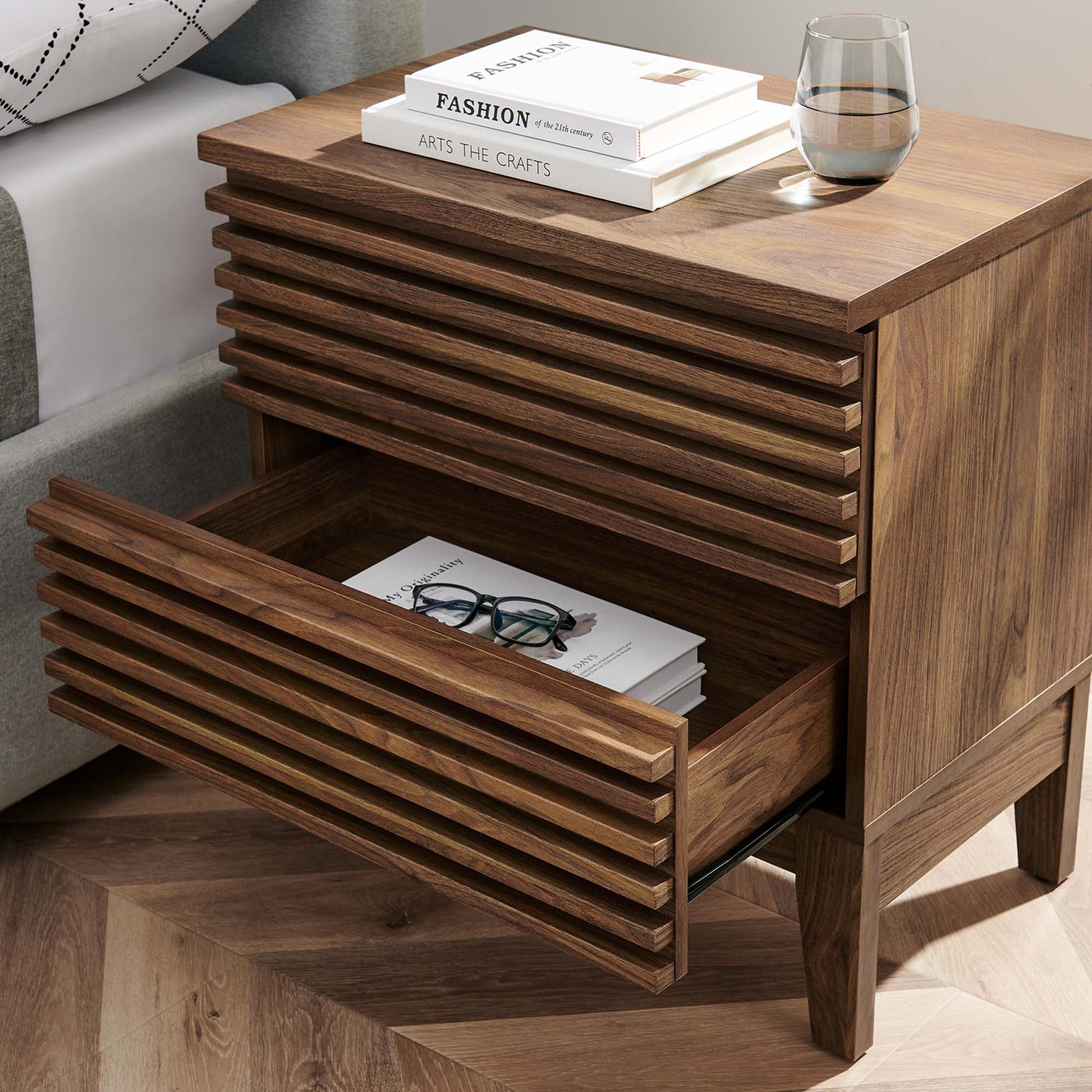 Walnut wood mid-century two-drawer nightstand; top with books and a glass, bottom drawer with magazines.