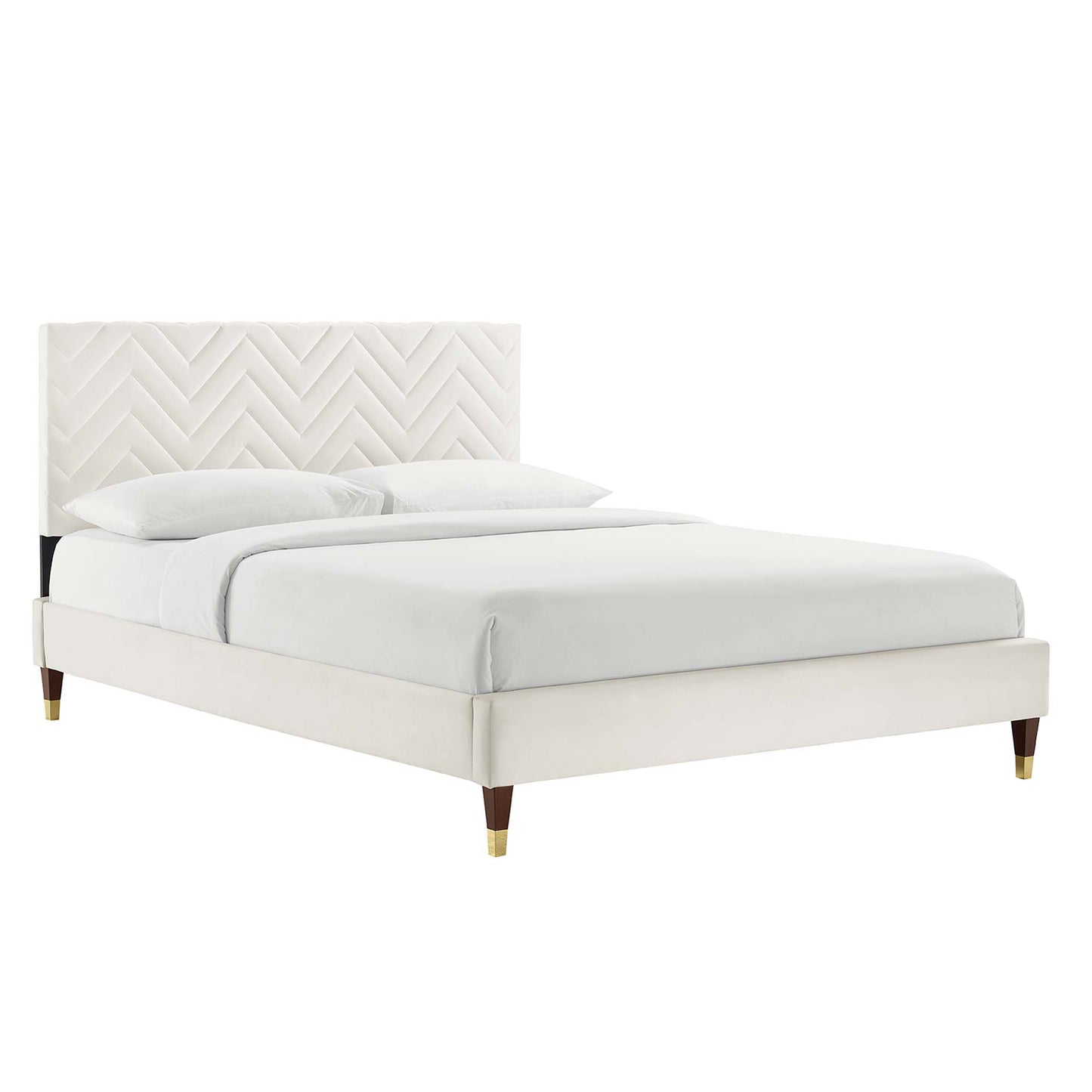 White upholstered platform bed with chevron tufted headboard, tapered legs with brass tips, and white linens.