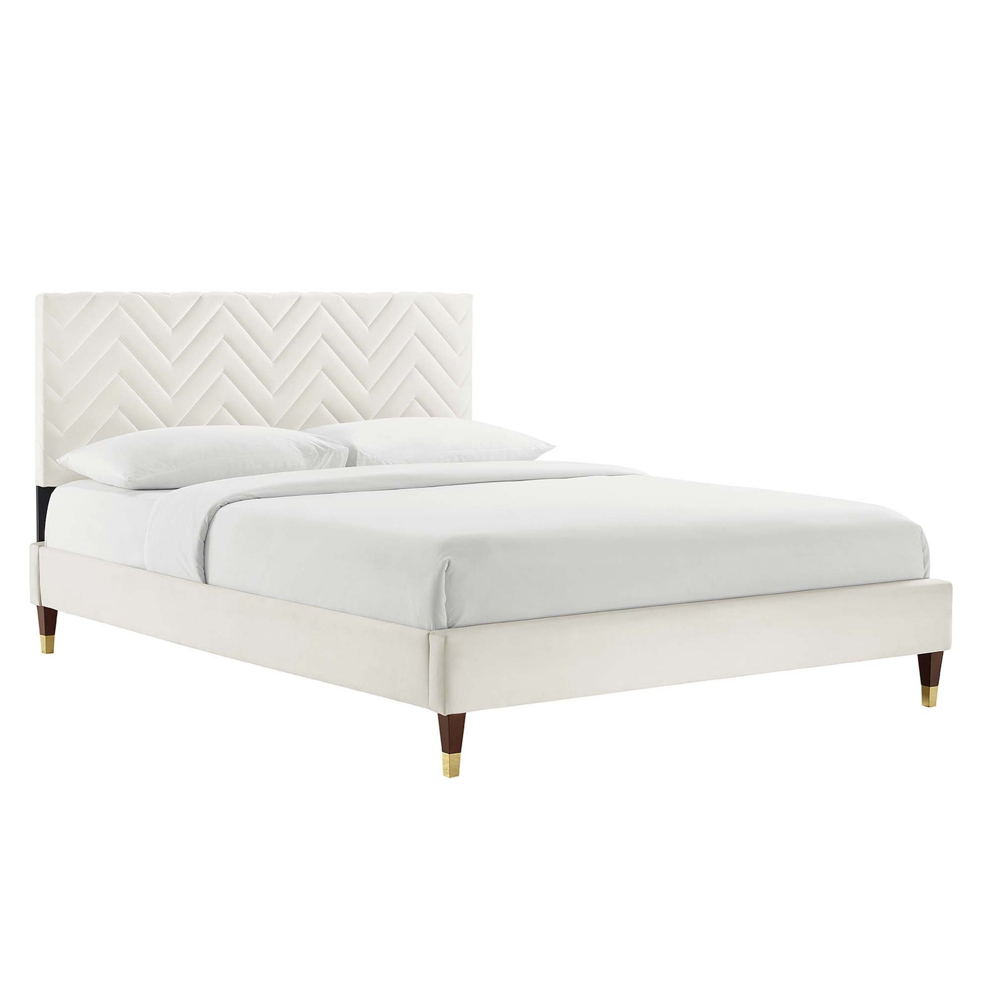 White upholstered platform bed with chevron tufted headboard, tapered legs with brass tips, and white linens.
