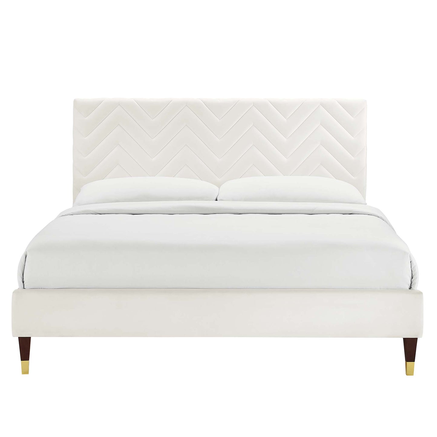 Cream upholstered platform bed with chevron-patterned headboard, white bedding, dark wooden legs with brass caps