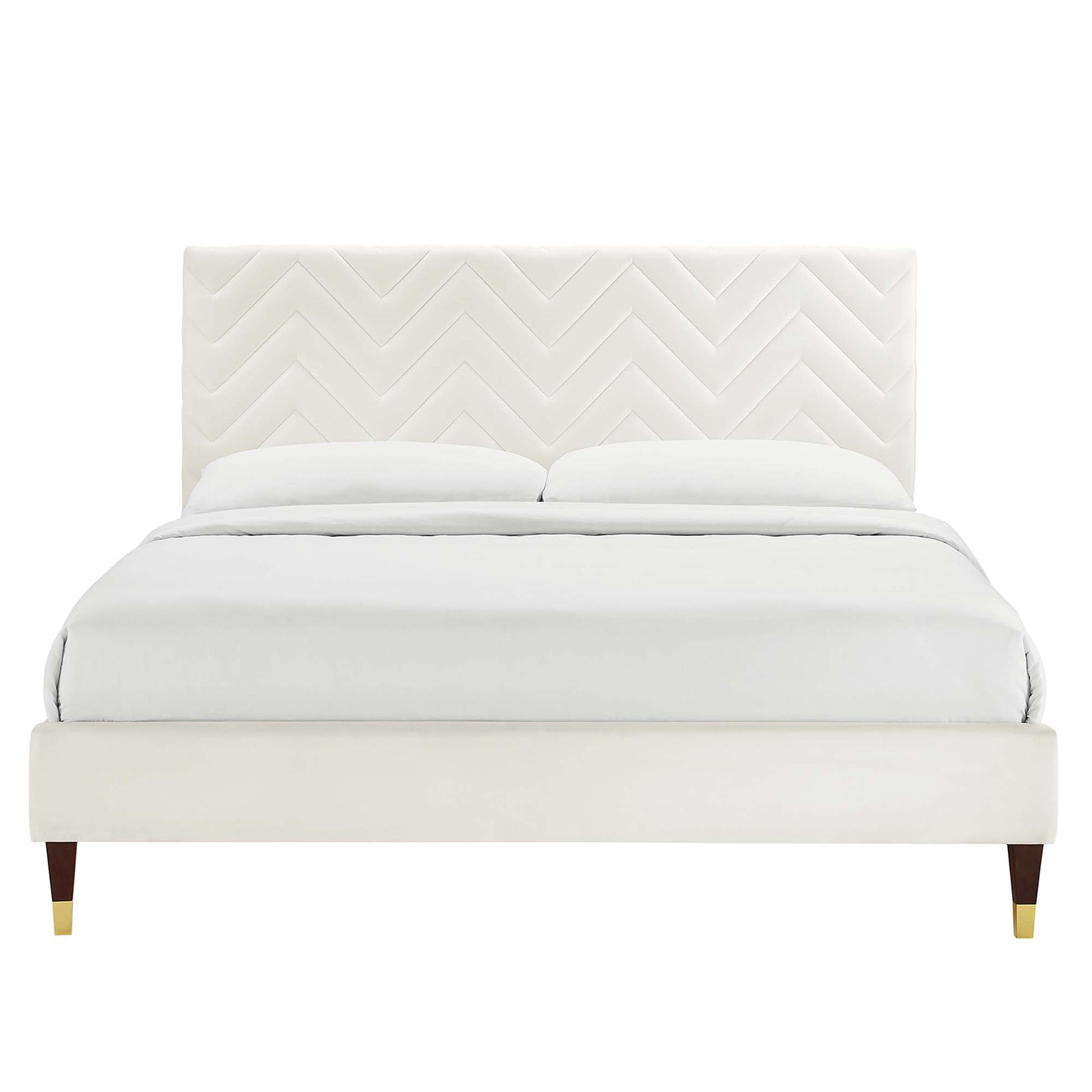 Cream upholstered platform bed with chevron-patterned headboard, white bedding, dark wooden legs with brass caps