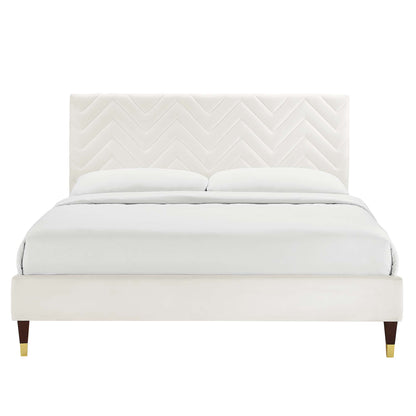 Cream upholstered platform bed with chevron-patterned headboard, white bedding, dark wooden legs with brass caps