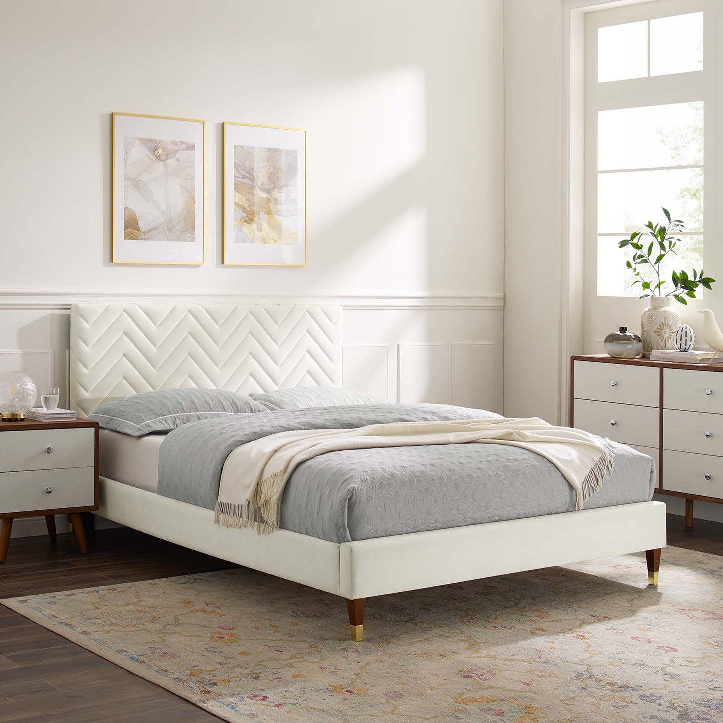 White platform bed with chevron headboard, grey bedding and beige throw; bright modern bedroom with nightstands and dresser.