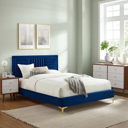 Navy velvet bed with channel-tufted headboard and gold legs, white bedding and a gray throw.