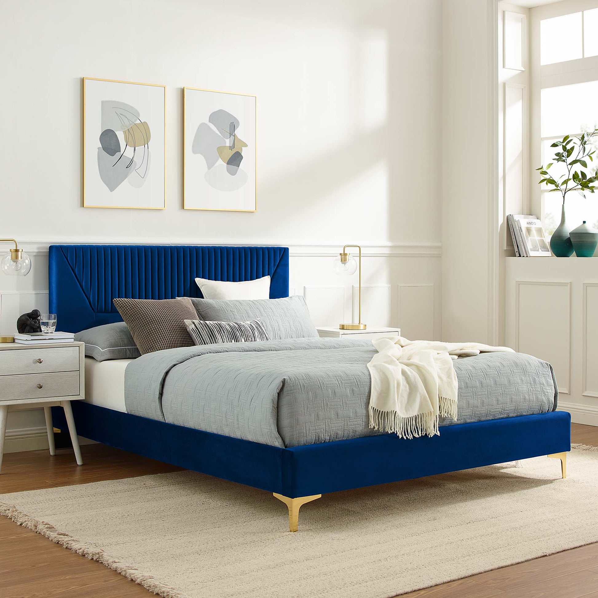 navy velvet twin platform bed with tall channel-tufted headboard, grey bedding, beige throw, gold legs, white walls, nightstands, abstract art.