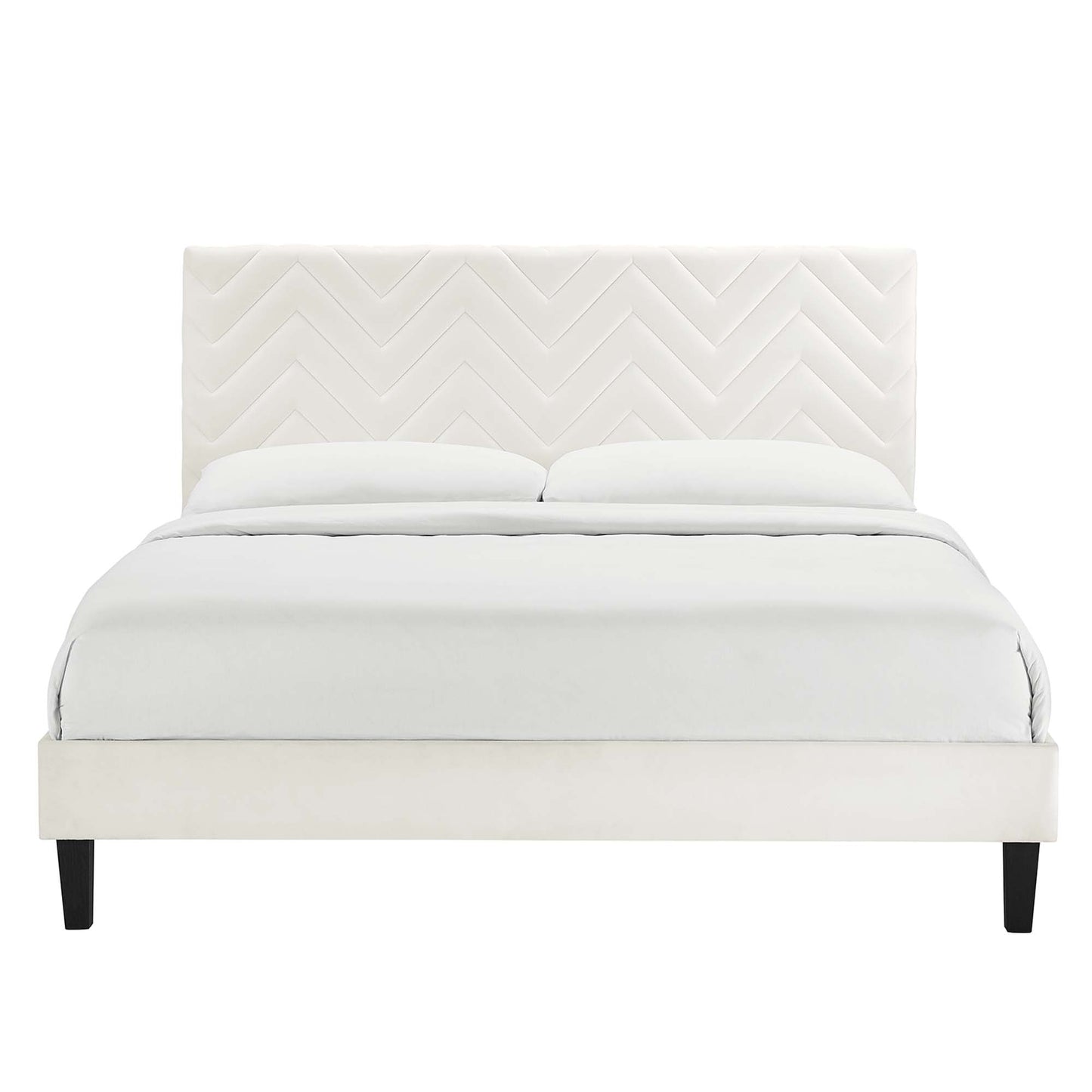 White upholstered bed with chevron quilted headboard, low-profile frame and dark feet, dressed in white bedding.
