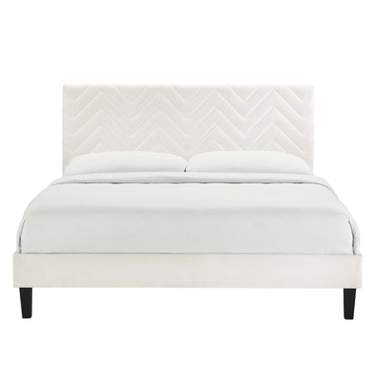 White upholstered bed with chevron quilted headboard, low-profile frame and dark feet, dressed in white bedding.